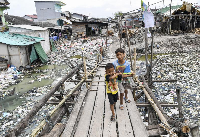 Dua anak berjalan meniti jembatan kayu yang penuh sampah di sekitarnya, di kawasan Kalibaru, Cilincing, Jakarta Utara, Rabu (8/6/2022). (ANTARA FOTO/M Risyal Hidayat)